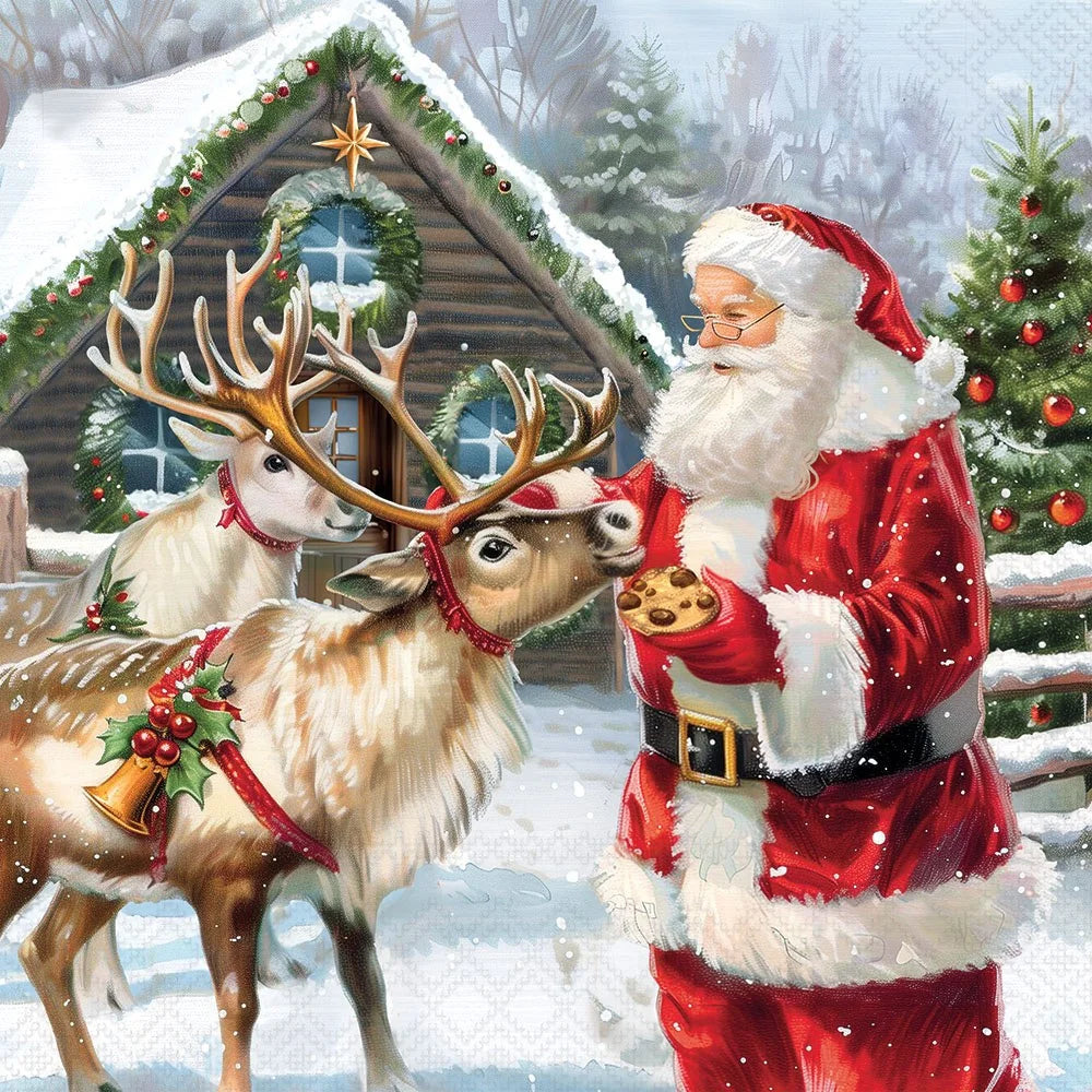 A festive winter scene showing Santa Claus in a red suit with white fur trim standing in the snow beside two reindeer in front of a snow-covered cabin. One reindeer is offering a cookie to Santa, and Christmas trees with red ornaments are visible in the background.