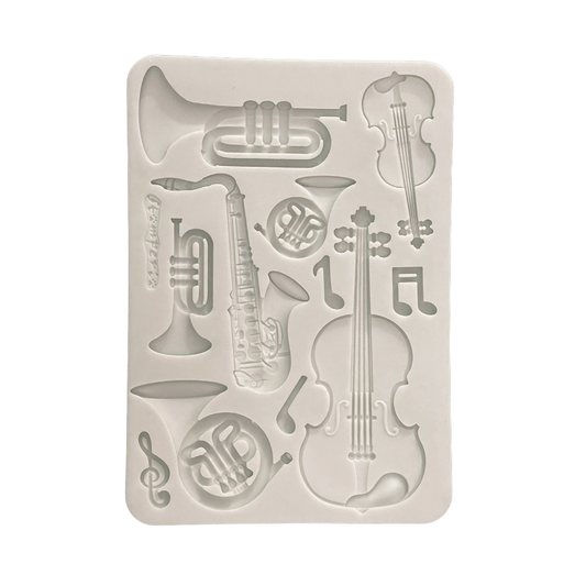 A rectangular white silicone mold featuring embossed musical instruments and notes, including a cello, trumpet, saxophone, French horn, and treble clef.