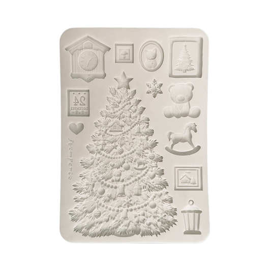 A rectangular silicone mold with Christmas-themed embossed designs, including a large decorated Christmas tree, a teddy bear, a rocking horse, a cuckoo clock, snowflakes, and small framed illustrations.