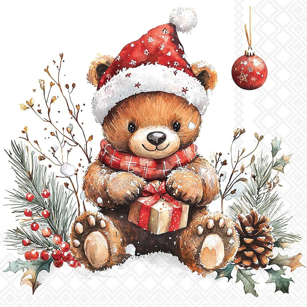 A festive watercolor-style illustration of a brown teddy bear wearing a red Santa hat with white trim and a red plaid scarf, sitting in snow and holding a wrapped gift. The scene includes pine branches, berries, holly leaves, a pinecone, and a hanging ornament on a white background.