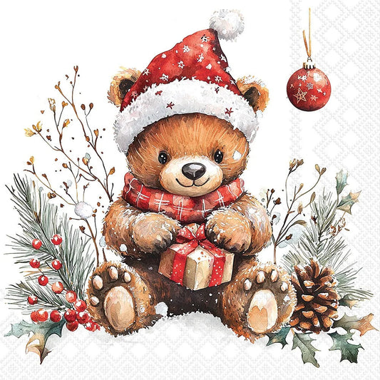 A festive watercolor-style illustration of a brown teddy bear wearing a red Santa hat with white trim and a red plaid scarf, sitting in snow and holding a wrapped gift. The scene includes pine branches, berries, holly leaves, a pinecone, and a hanging ornament on a white background.